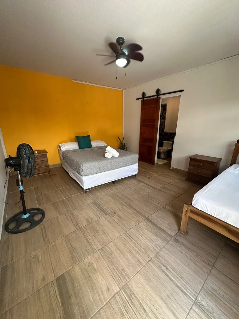 Room Three — bright bedroom with a sunlit yellow accent wall
